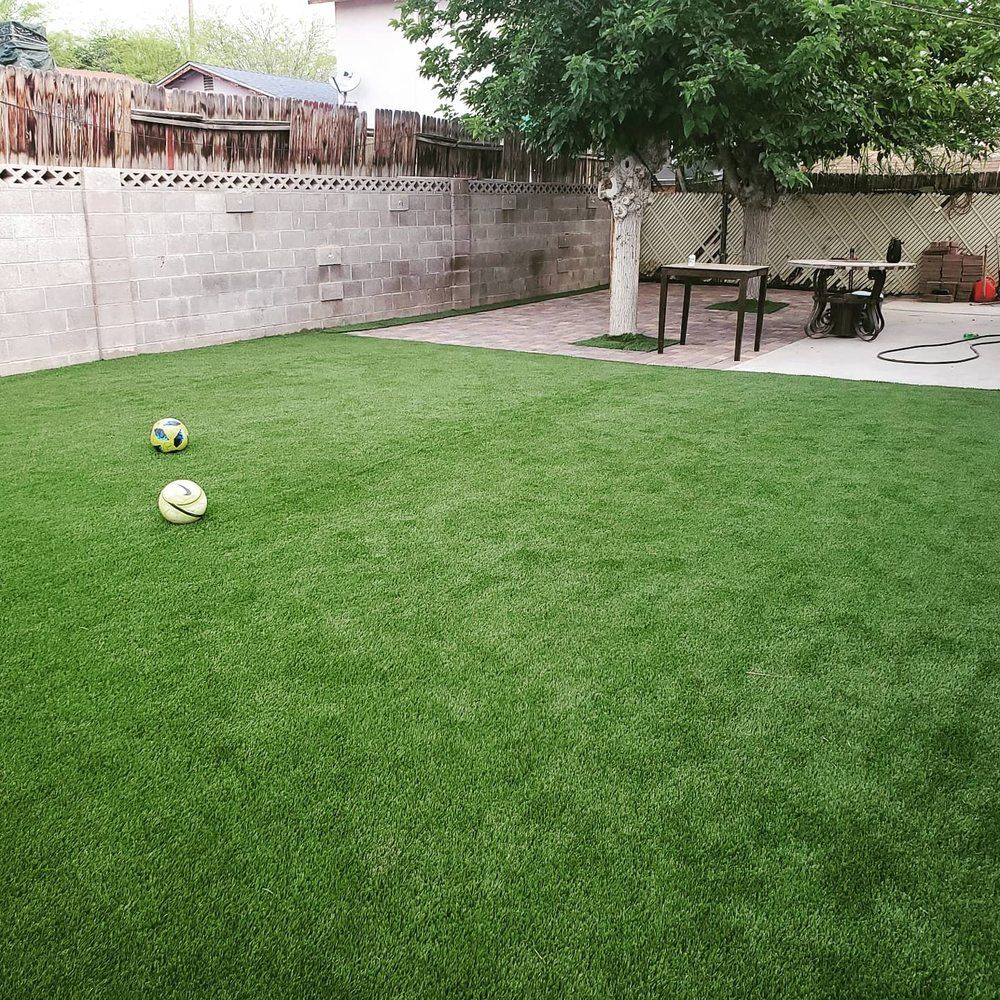 Two soccer balls are sitting on top of a lush green lawn in a backyard.
