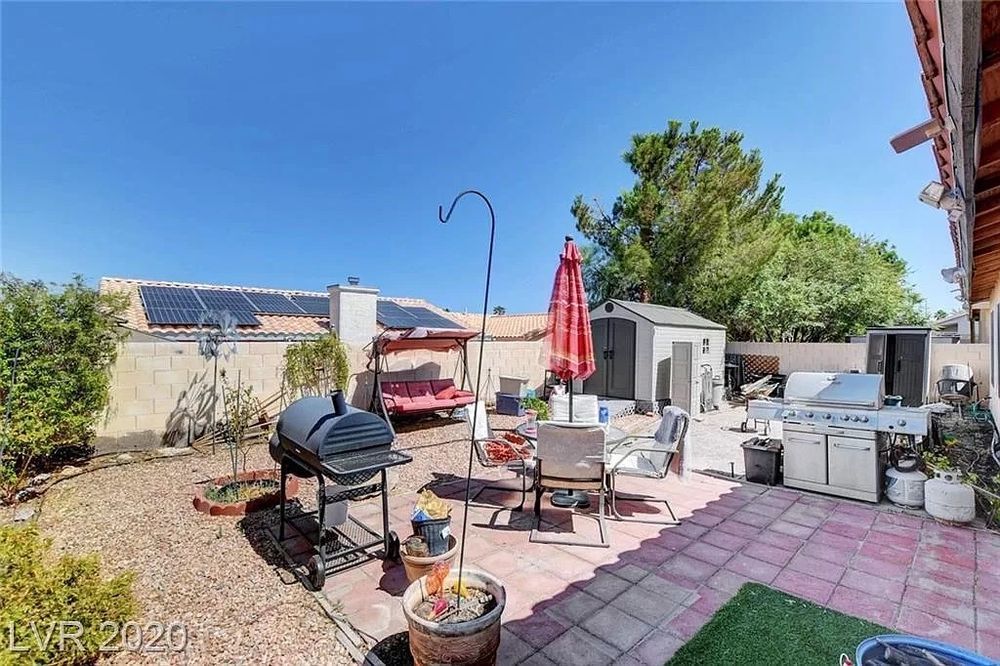 A patio with a grill , umbrella , chairs , and a shed.
