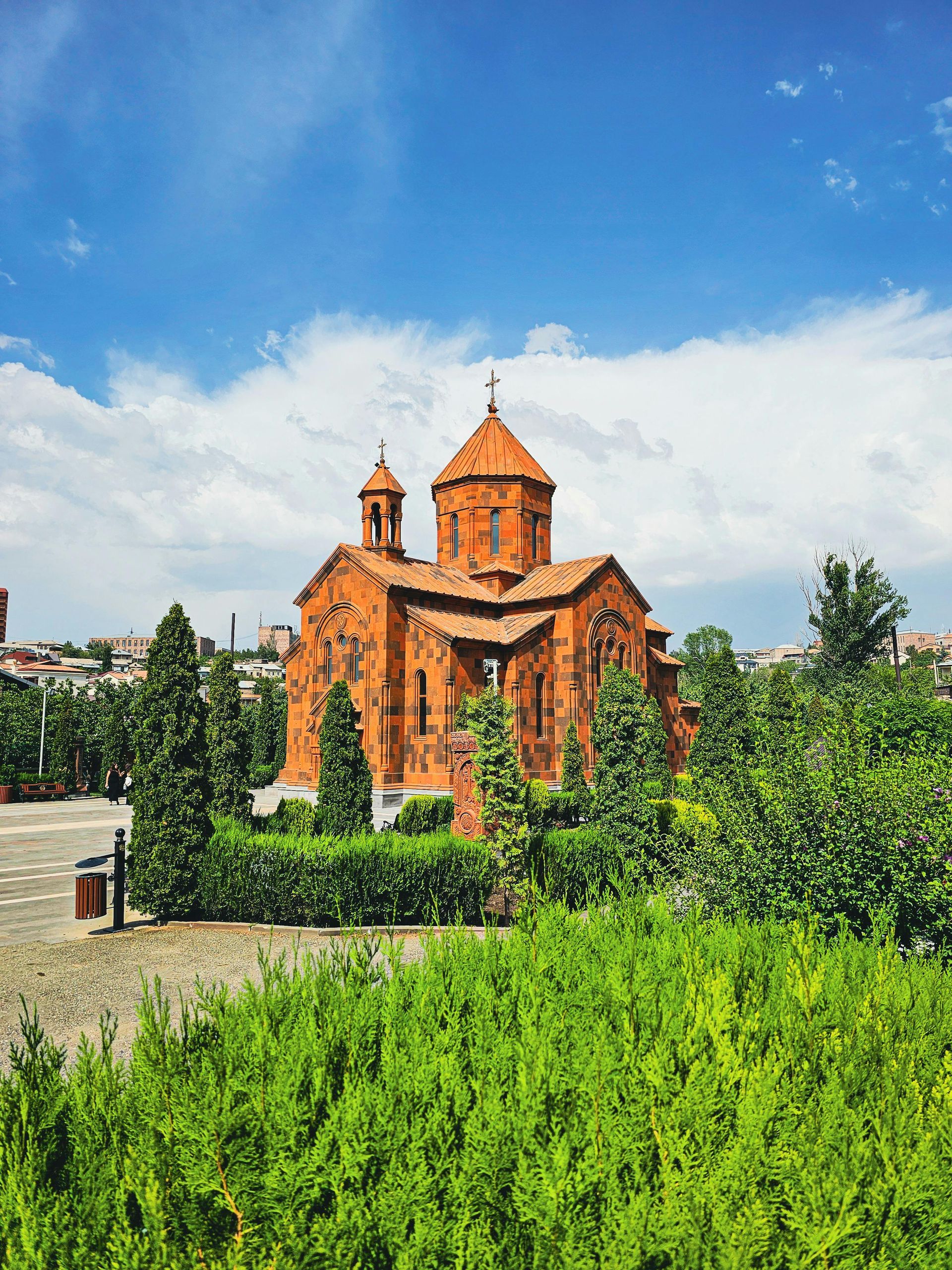A large red brick church is surrounded by trees and bushes.