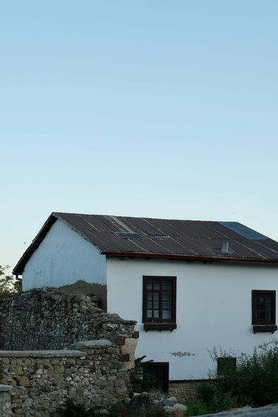 White house with dark window frames and a tiled roof against a clear blue sky.