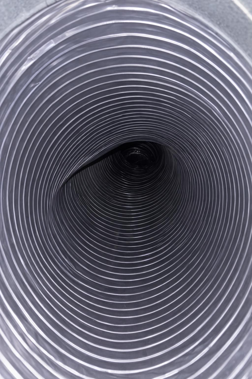Inside view of a clean flexible, ribbed, silver and dark gray tube, disappearing into the darkness.