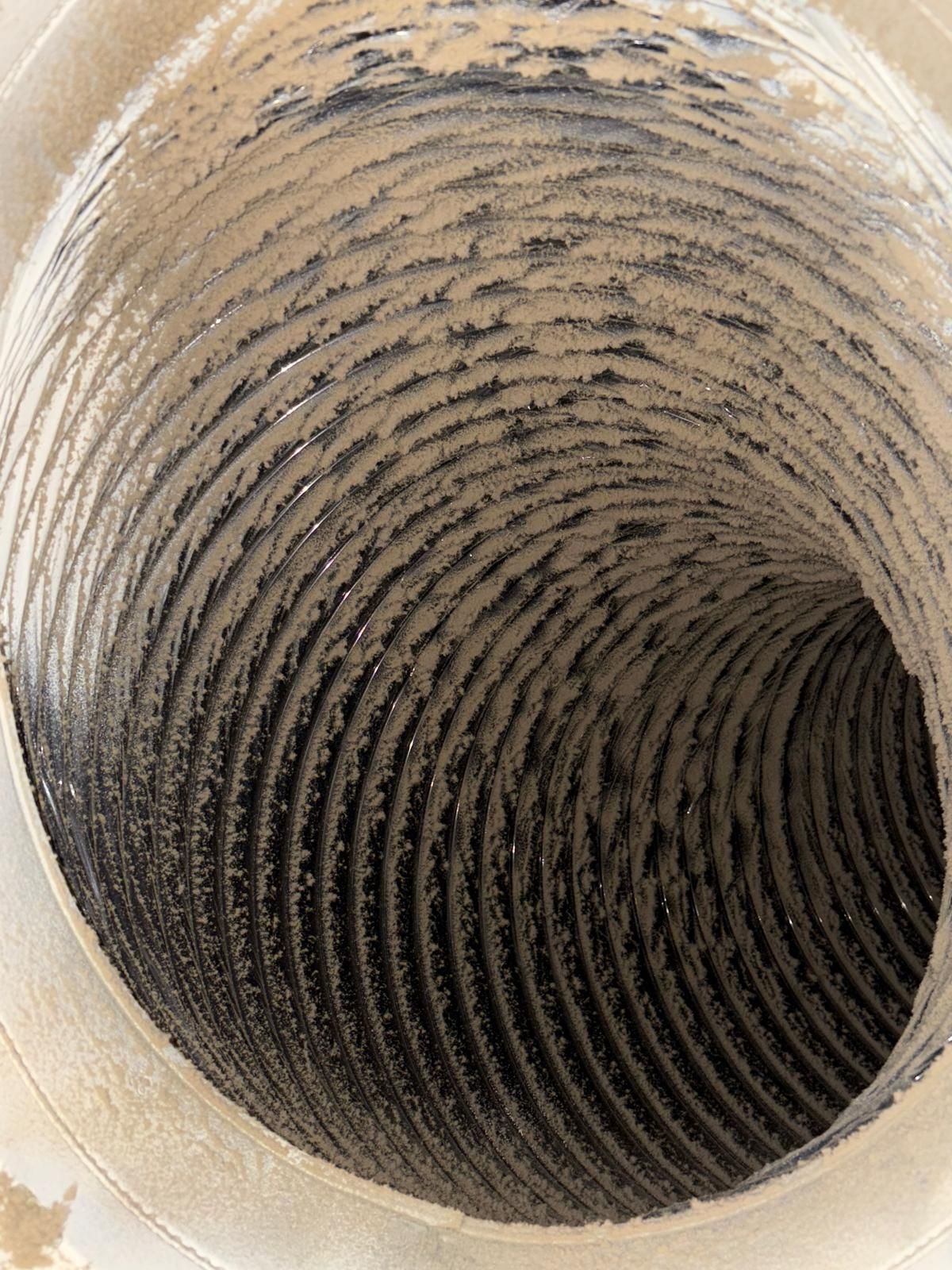 Inside view of a dusty, flexible duct, with a spiral-shaped interior covered in debris.