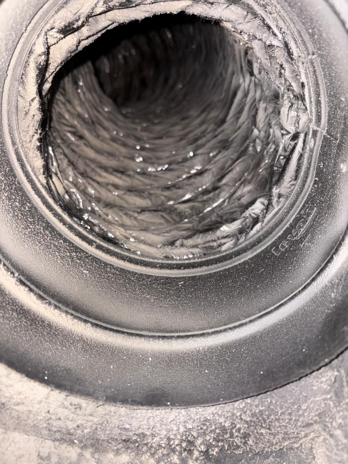 View inside a dusty flexible duct. The interior has a corrugated texture, surrounded by a black plastic ring.