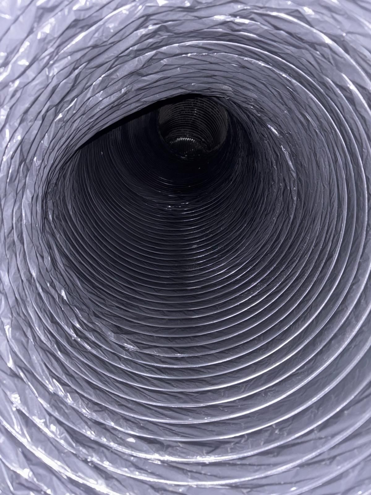 Inside view of a flexible metallic duct, appearing as a dark tunnel, with circular ridged interior.