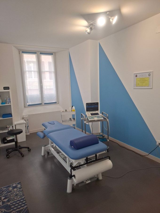 Une table de massage bleue est posée dans une pièce à côté d'une fenêtre.