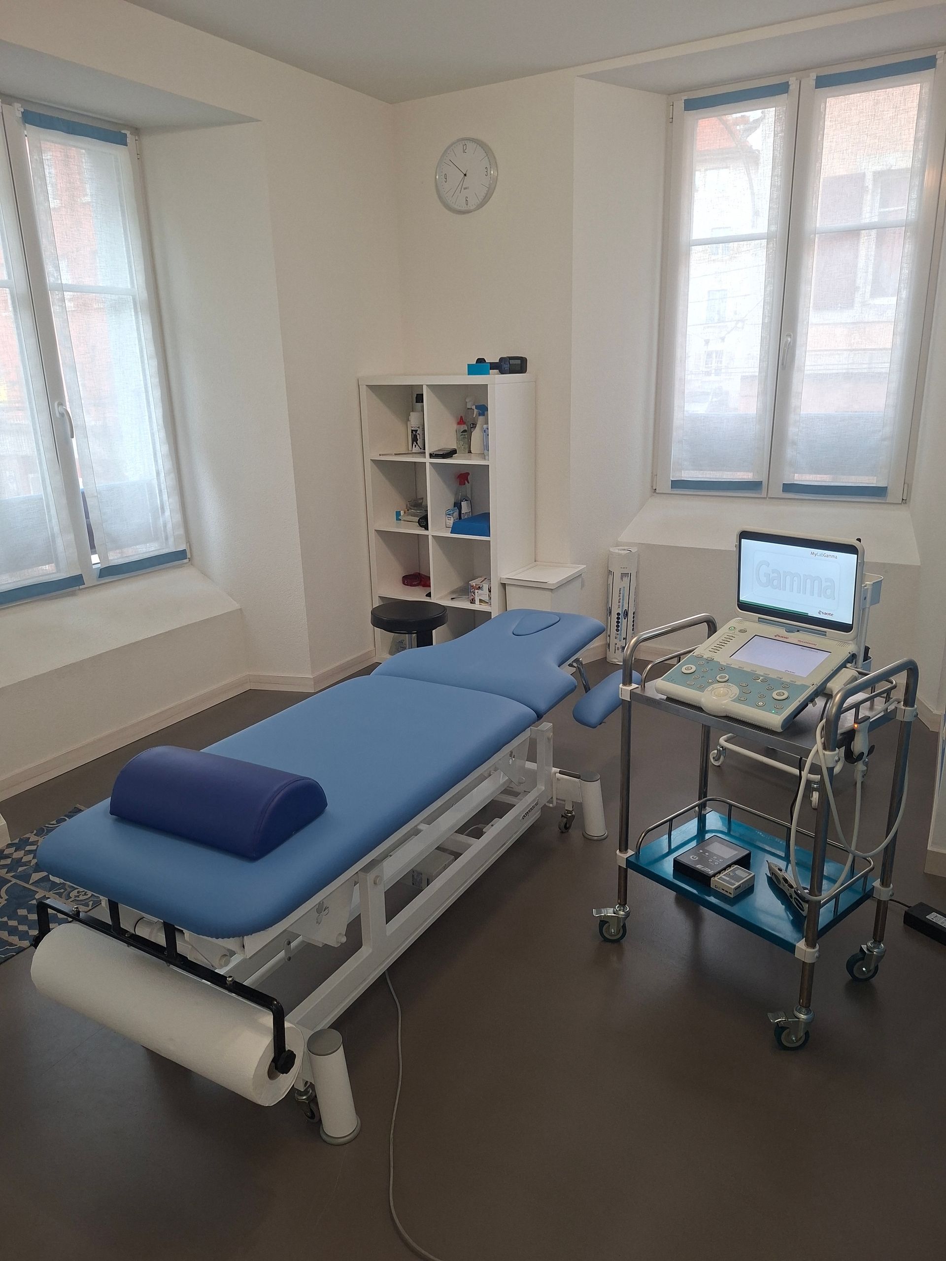 Une chambre avec un table bleu et un ordinateur echographe sur un chariot.