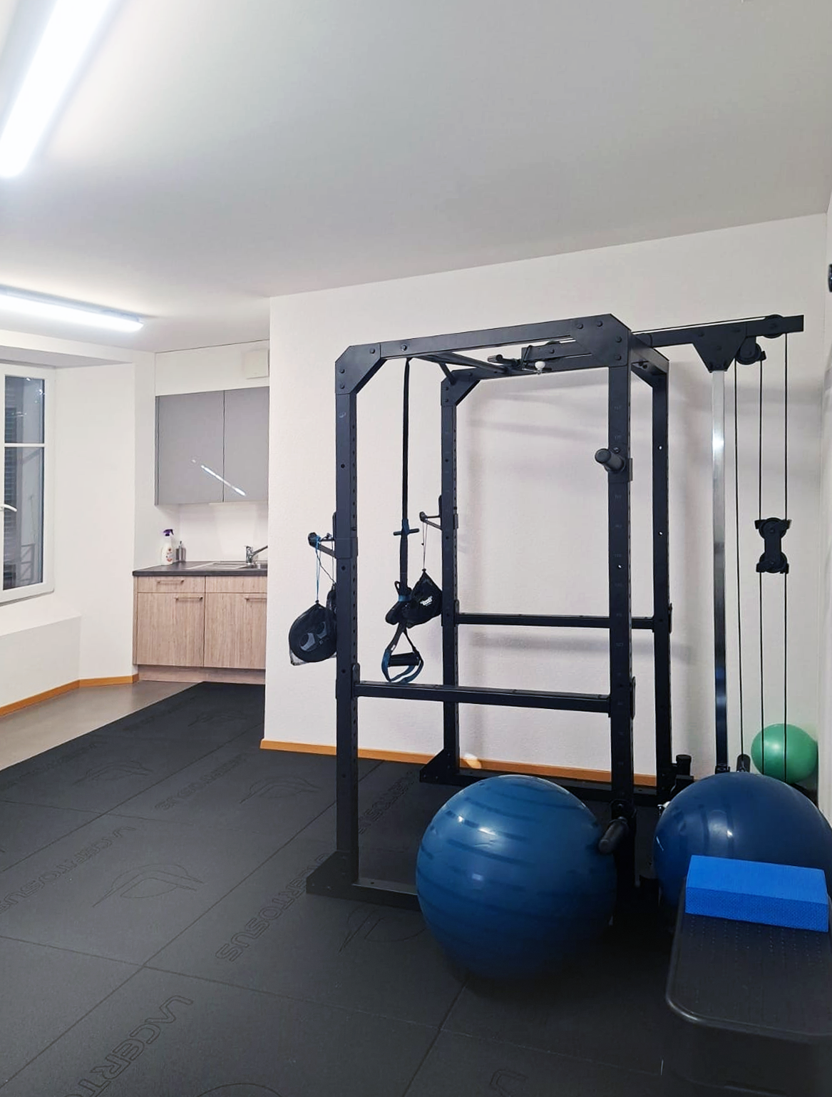 Une salle de sport avec un support à squat, des ballons d'exercice et un banc.