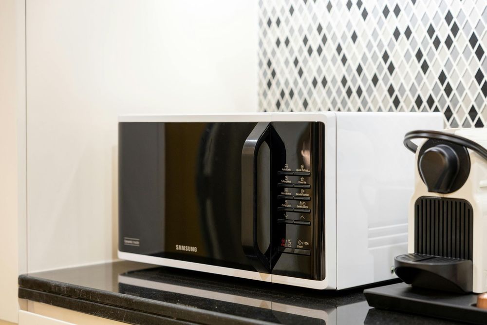 A white microwave with a black door and handle sits on a black countertop next to a coffee machine.