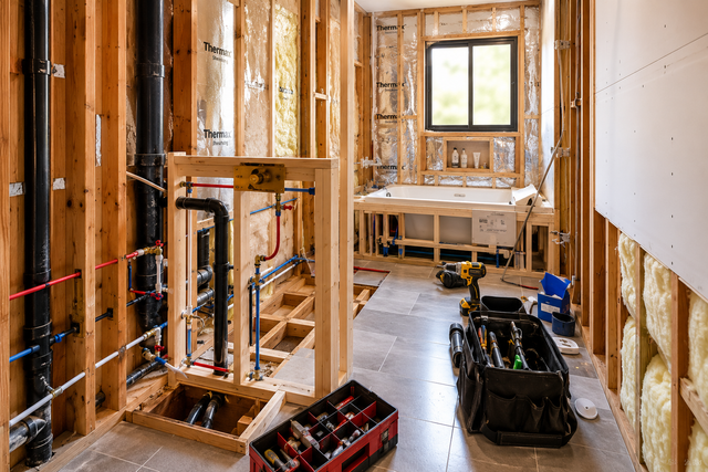 Unfinished bathroom under construction with exposed studs, plumbing, window, and tools on the floor