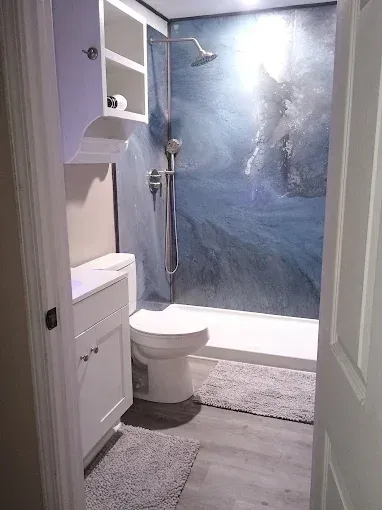 Small modern bathroom with a blue-tiled shower, white fixtures, and gray flooring.