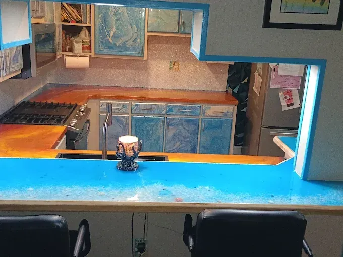 A kitchen with blue countertops and cabinets, a stove, a sink, and a countertop bar with stools.