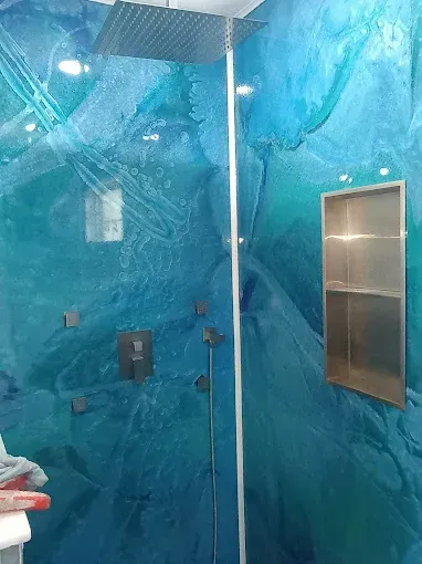 Blue and teal tiled shower with glass door and built-in shelf. Silver shower head and fixtures.