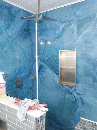 Blue marbled shower with stainless steel fixtures and shelf.