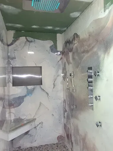 Shower with marbled walls, built-in shelf, multiple showerheads, and a recessed panel.