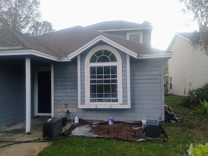Blue house with a large arched window. Brown roof, white trim. Overcast day.