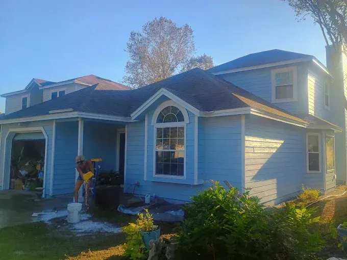 Blue house with white trim, a person washes a portion of the exterior. The sky is blue.