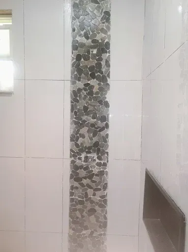 White tiled shower with a vertical strip of gray river stones.