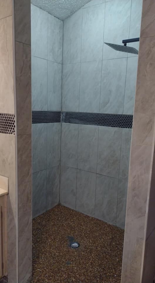 Shower stall with pebble floor, gray tile walls, and a black accent stripe.