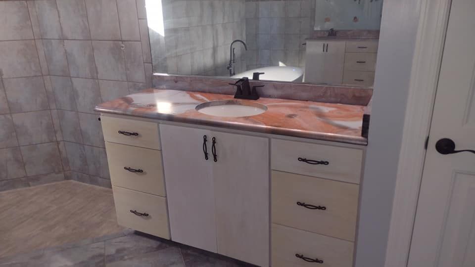 Bathroom vanity with cream cabinets, pink marble countertop, black hardware, and large mirror.