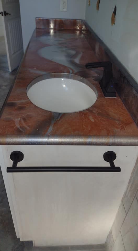 Bathroom vanity with copper-colored countertop, white sink, black faucet, and towel bar.