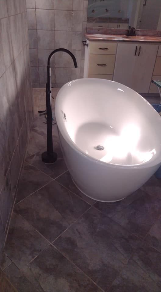 Freestanding white bathtub with black faucet, set in a tiled bathroom.