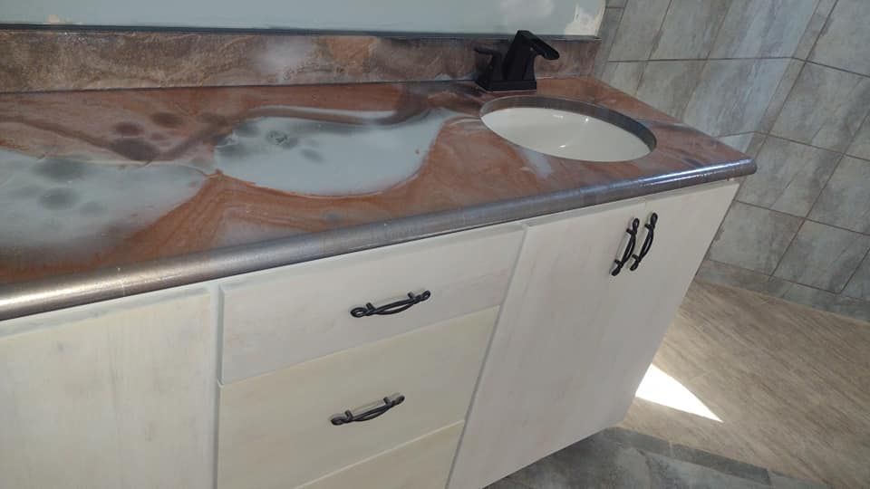 Bathroom vanity with white cabinets, brown and white countertop, black faucet, and oval sink.