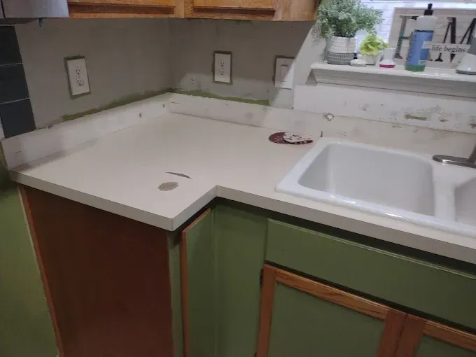 Kitchen countertop with sink and cabinets, showing damage and wear.