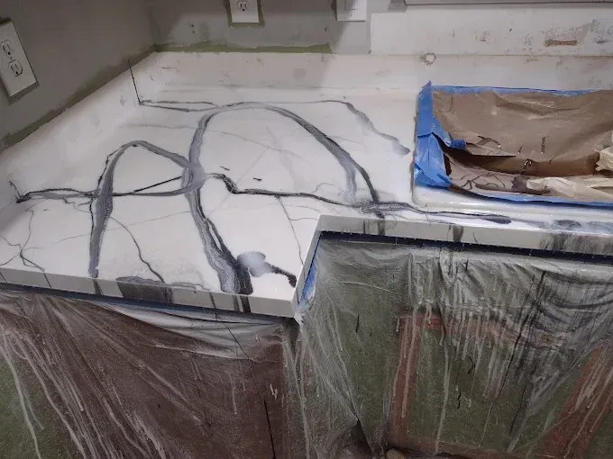 Kitchen countertop with gray veining and cabinet below covered in plastic.