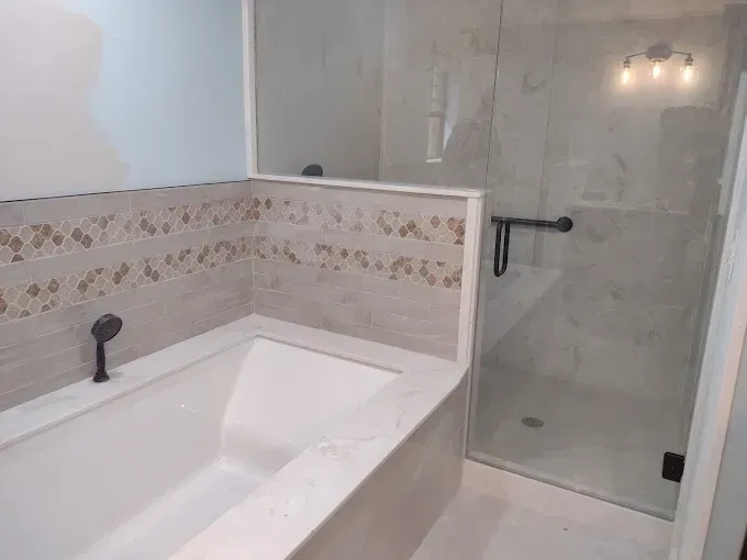 Bathroom with a tub and a glass shower. Beige tile accents and dark fixtures.