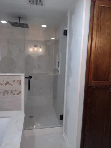 A modern, glass-enclosed shower in a bathroom, with white tiles and dark hardware.