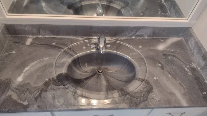 Dark grey swirled vanity with a round sink and faucet, beneath a mirror.