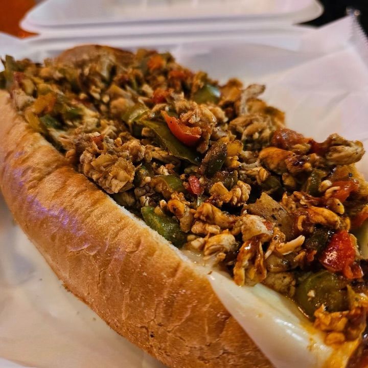 A sandwich with meat and vegetables on a bun in a styrofoam container