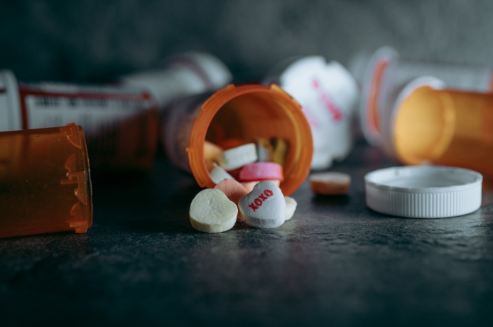 Open orange pill bottle spilling pills onto a surface. White and pink pills are visible.