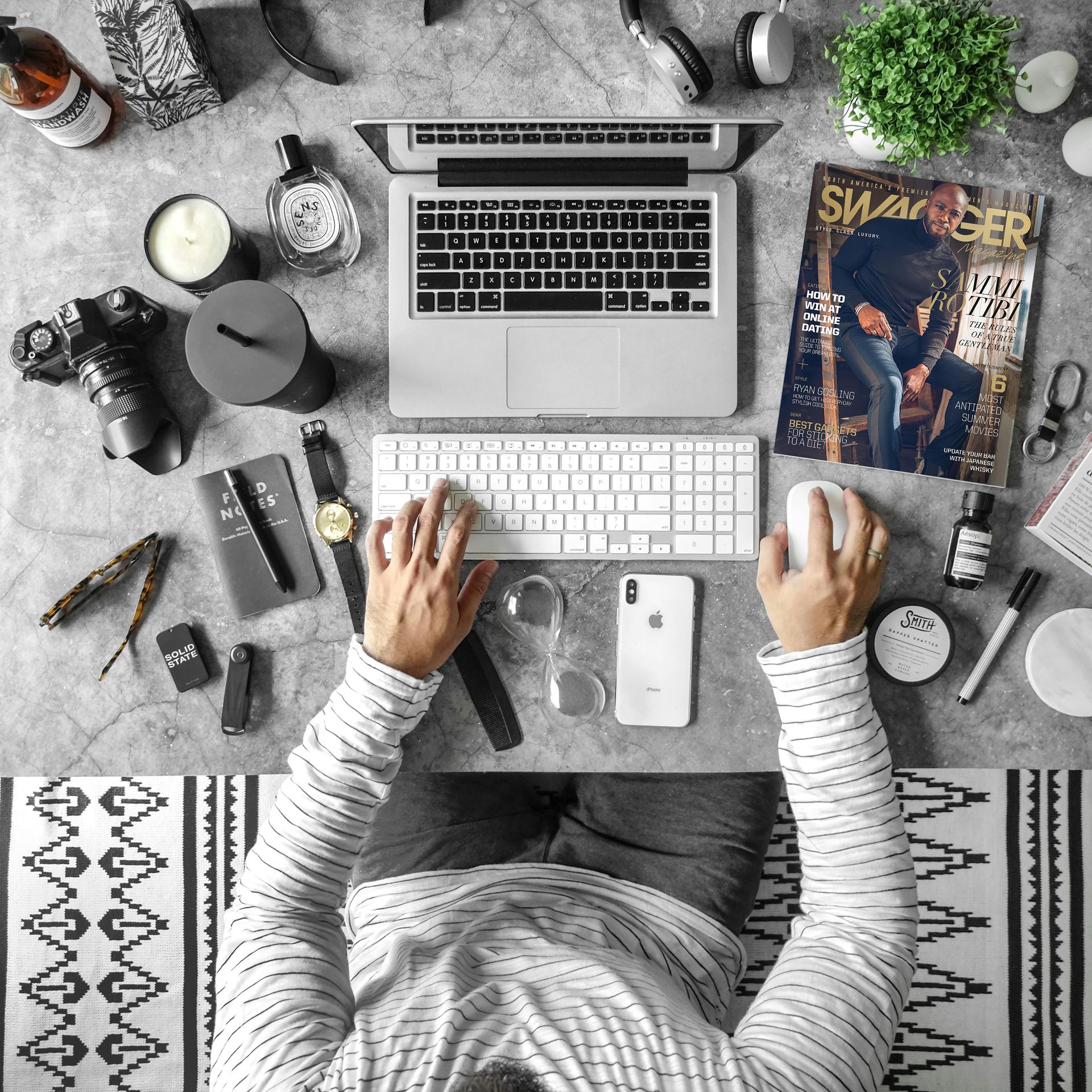 Person working on a laptop with desk accessories, including a camera, magazine, and plant.