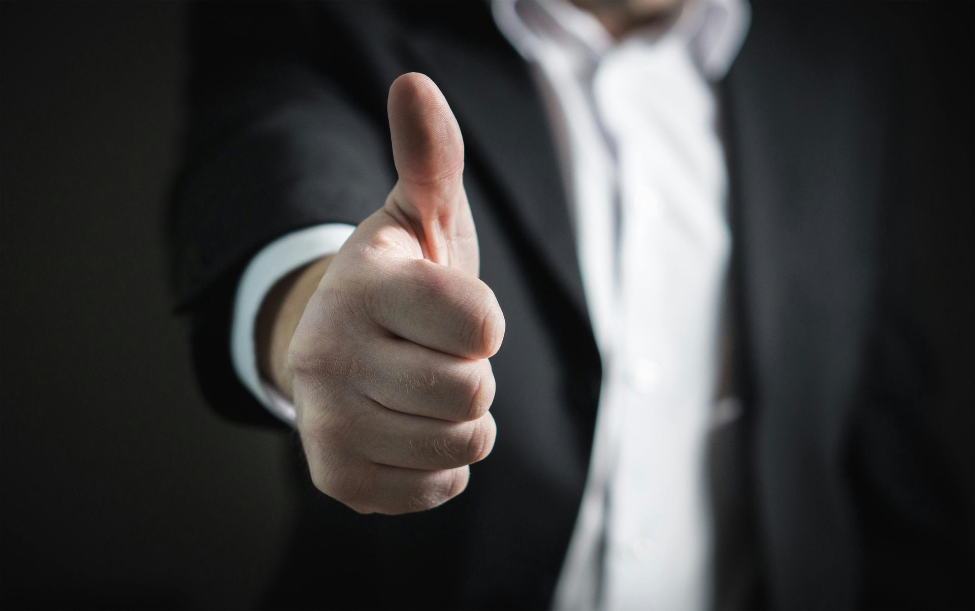 Person in a suit gives a thumbs-up, showing approval or agreement.