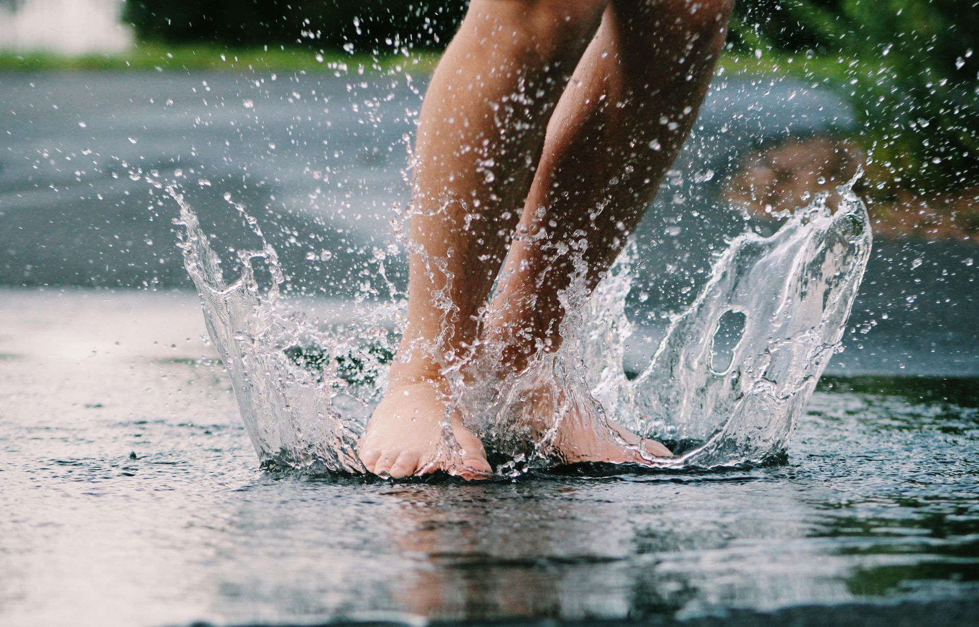 Bare feet splashing in a puddle, sending water droplets outward.