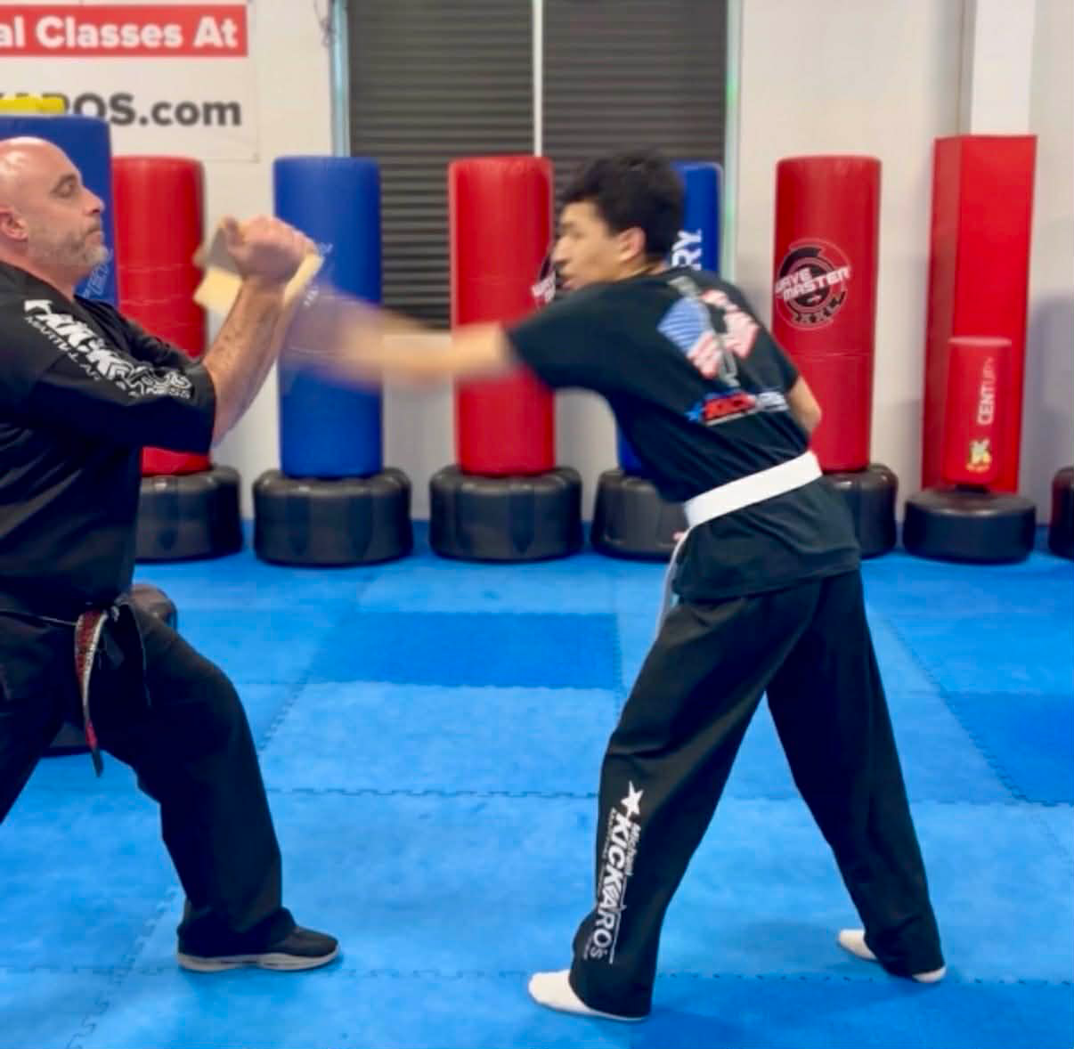 Martial arts student punching a board held by an instructor in a dojo.