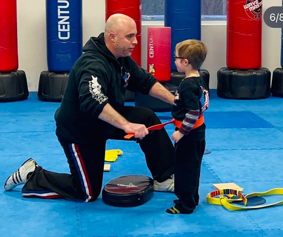 Man teaching a boy martial arts in a gym; he is adjusting the boy's belt.