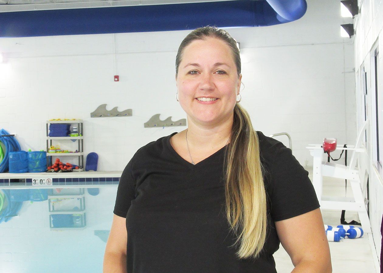 A woman in a black shirt is standing in front of a swimming pool.