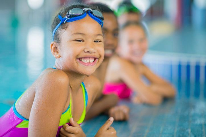 A young girl is giving a thumbs up in a swimming pool.