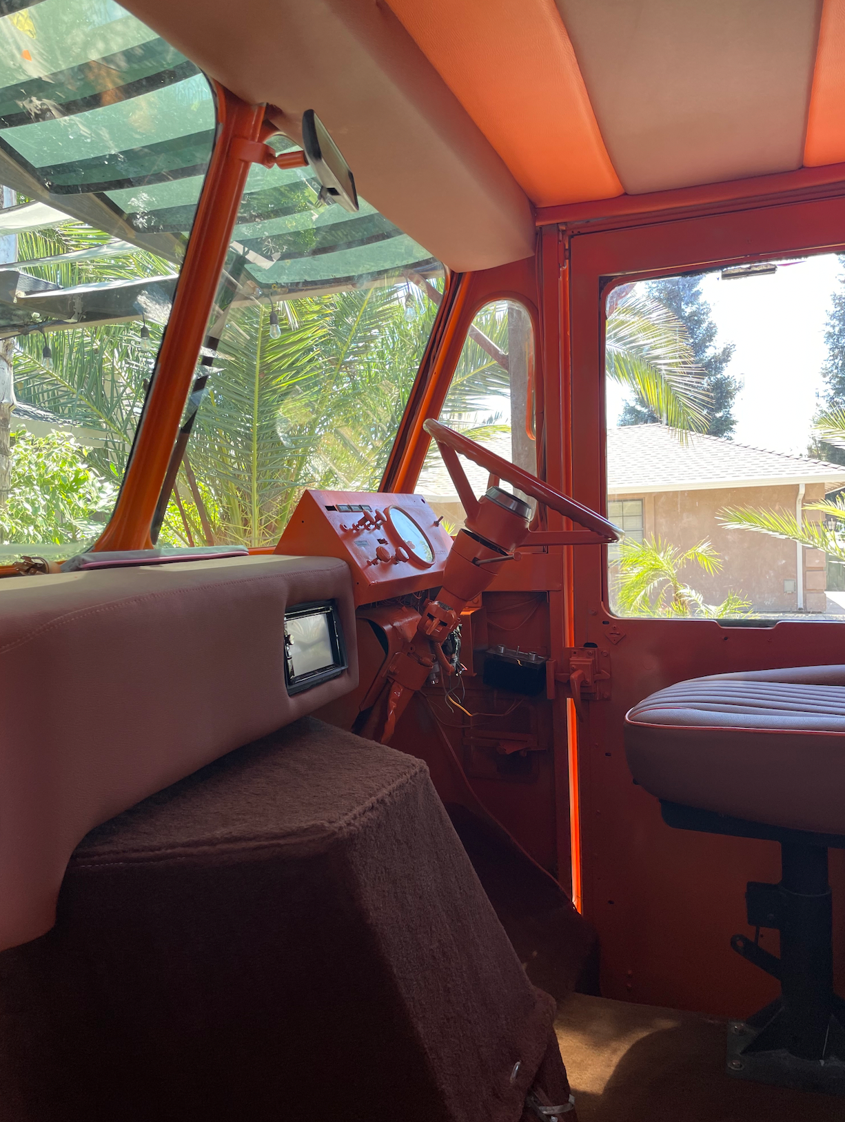 The inside of an orange vehicle with a steering wheel and a seat.