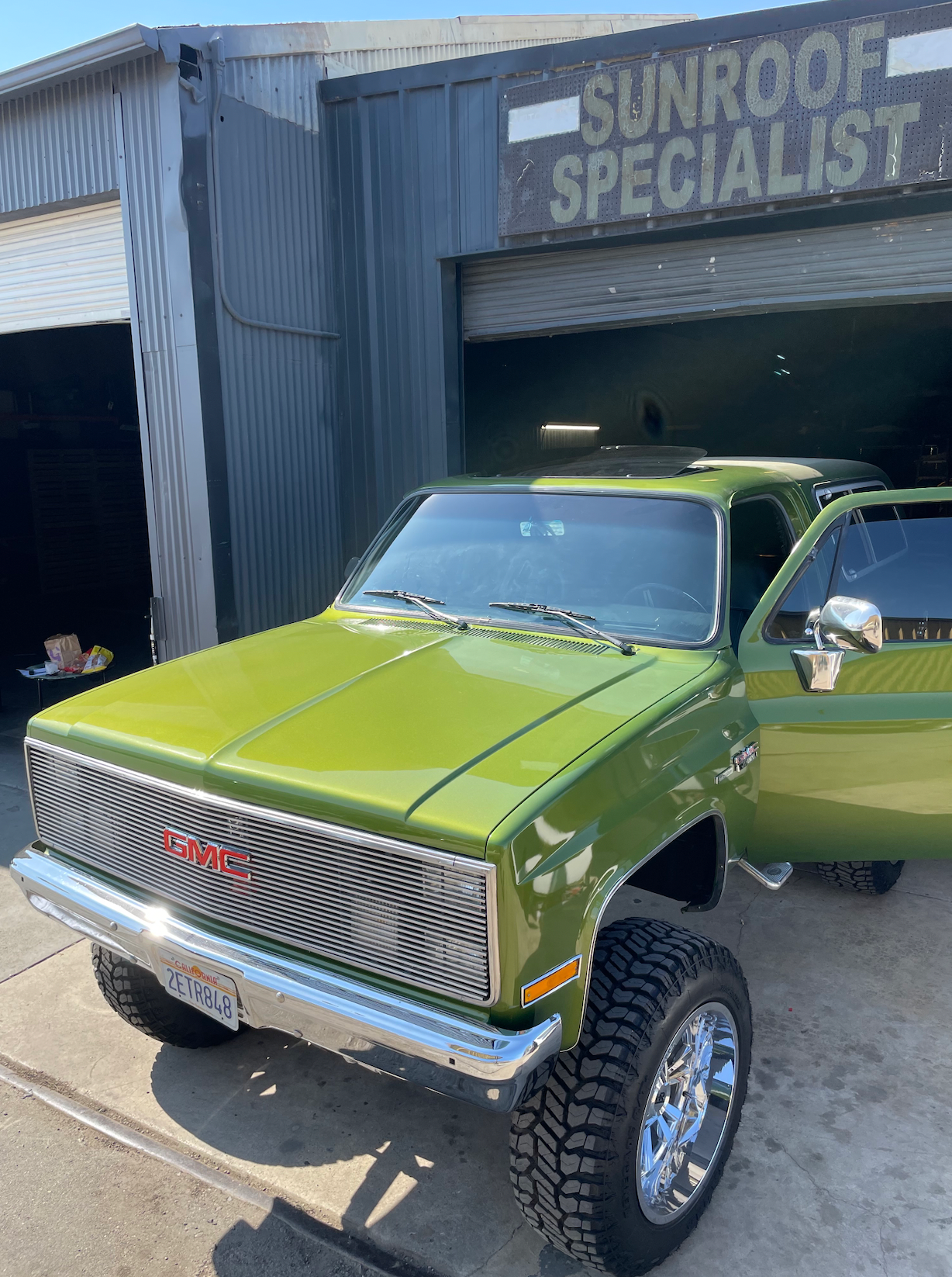 A green gmc truck is parked in front of a garage.