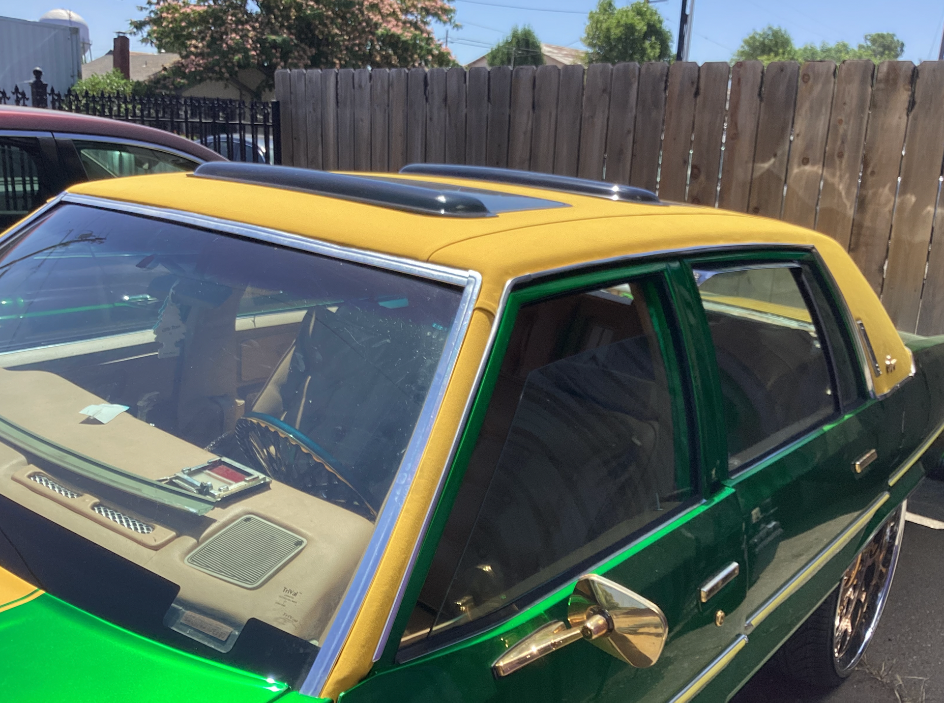 A green car with a yellow roof is parked in front of a wooden fence