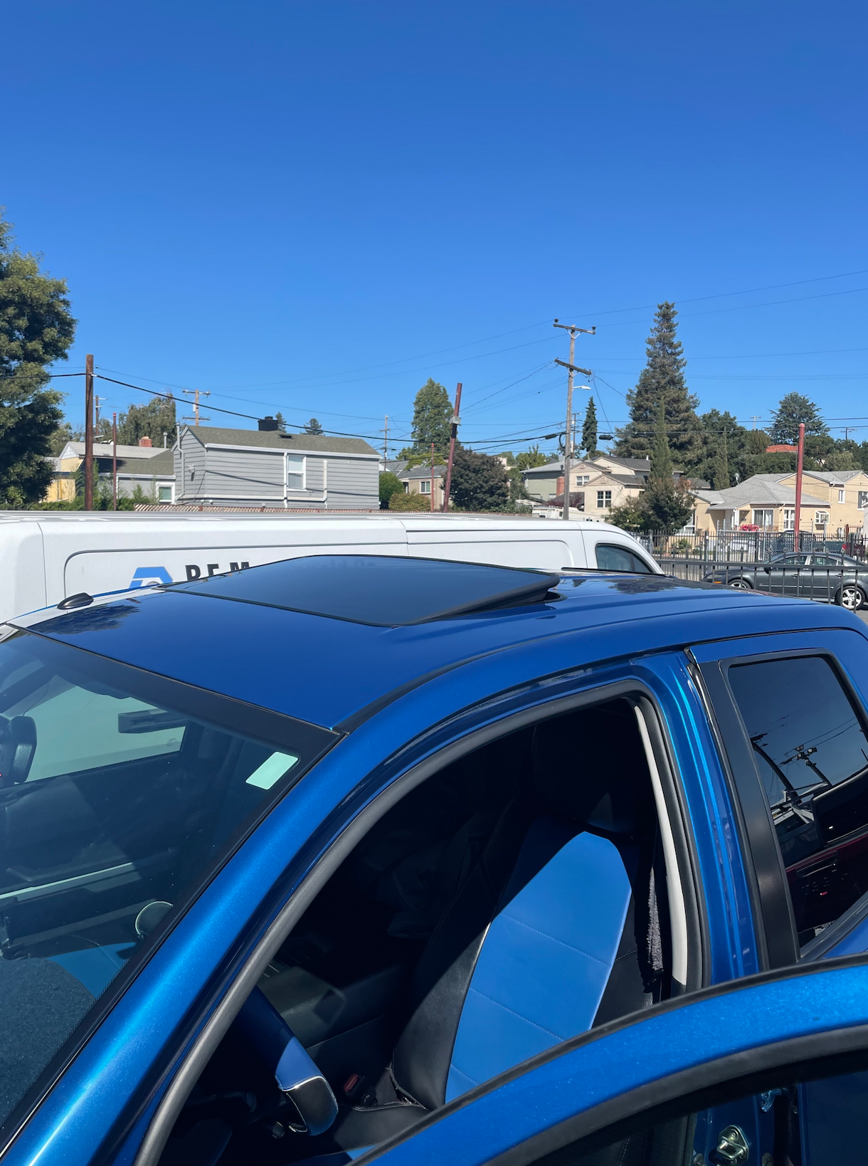 A blue car is parked in a parking lot with a white van in the background