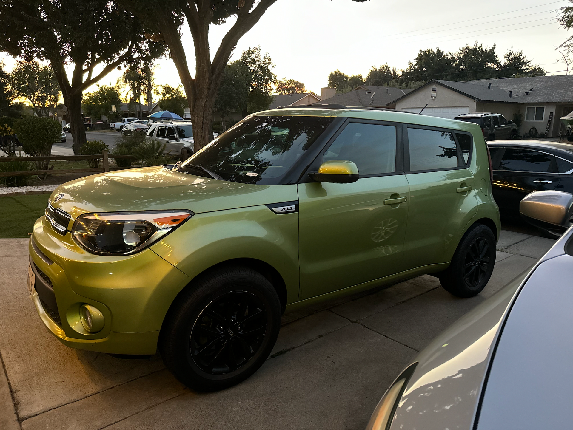 A green car is parked in a driveway next to other cars.