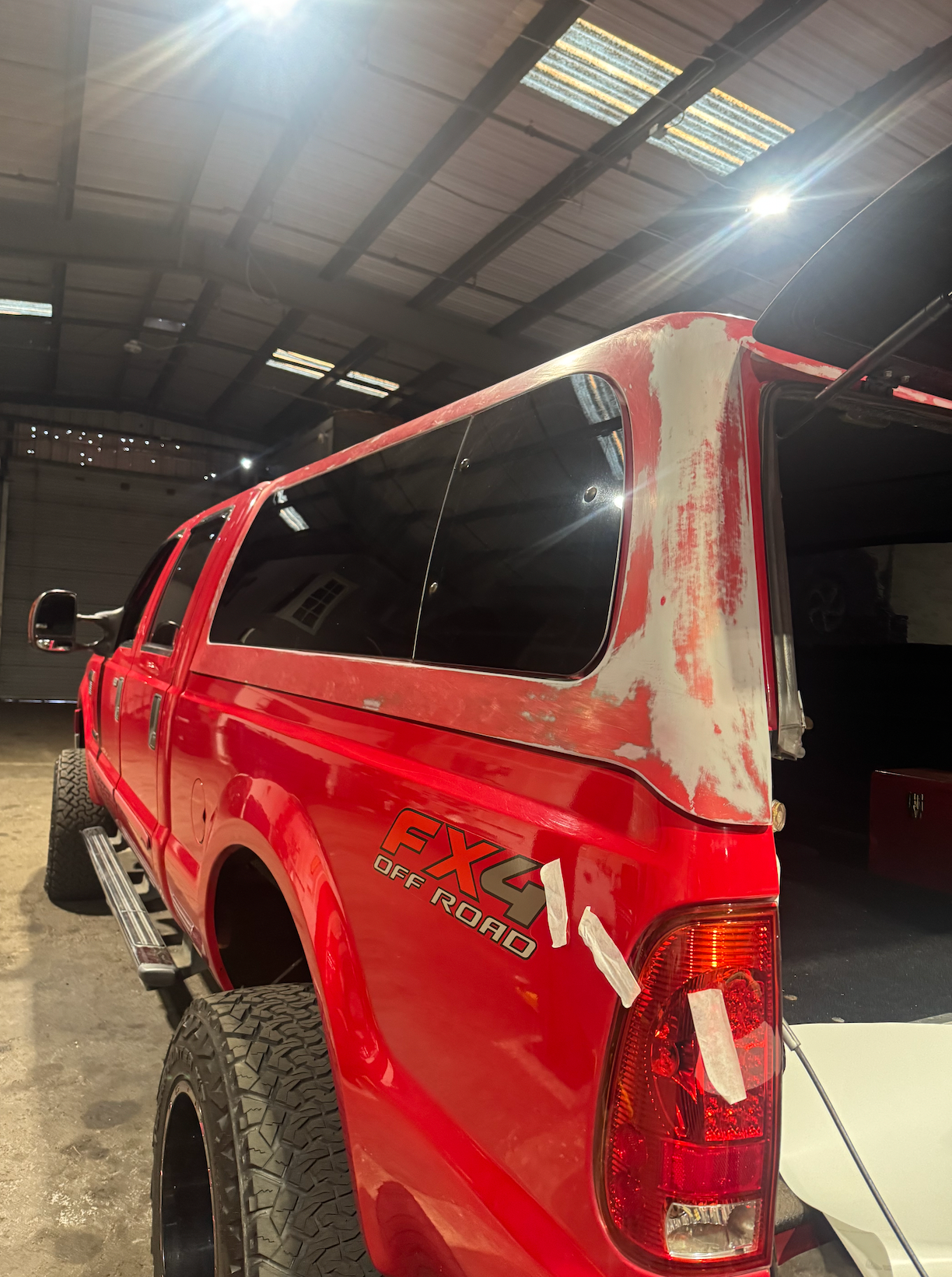 A red truck is parked in a garage with the back window missing.