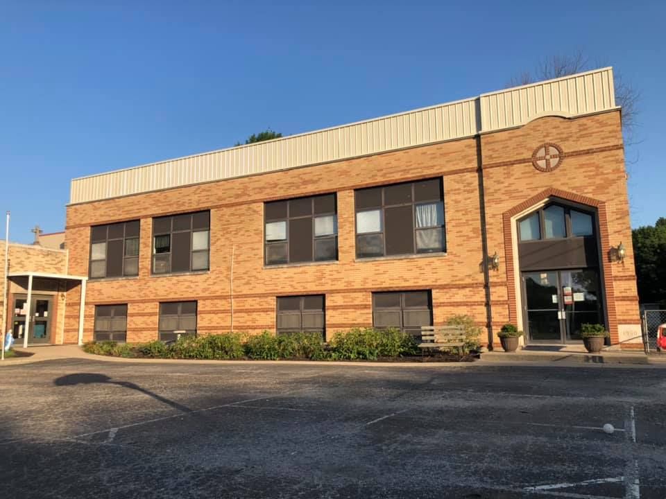 A large brick building with a lot of windows is sitting in a parking lot.