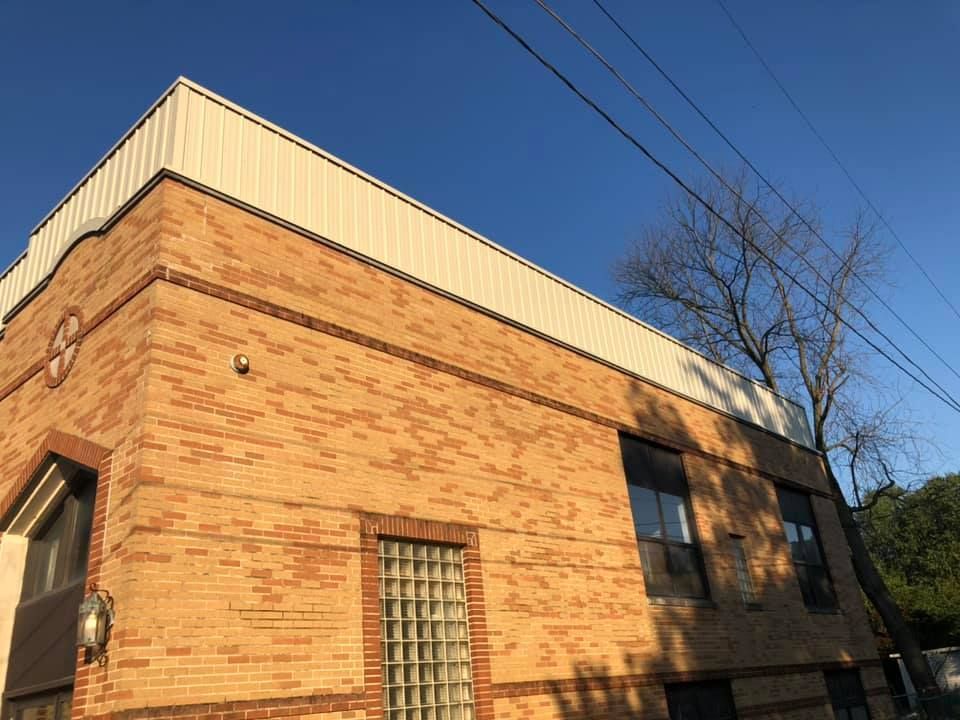 A brick building with a white roof and a tree in the background