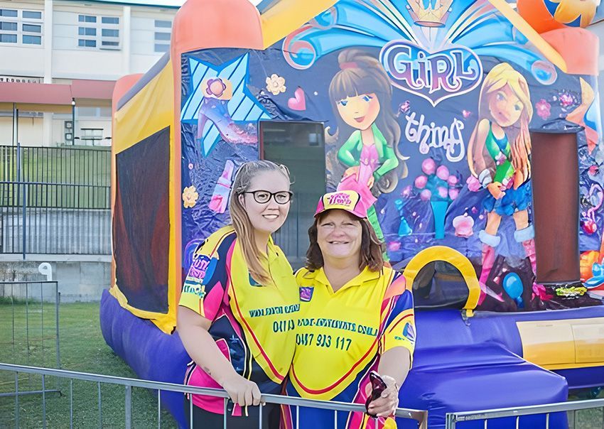 Two Women Are Posing for a Picture in Front of a Bouncy House — Fun Time Amusements in Gracemere, QLD