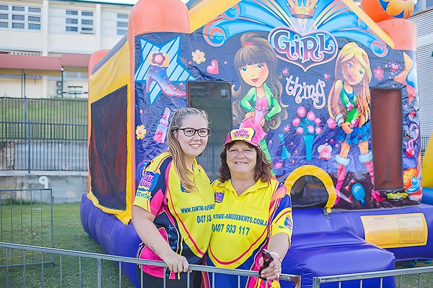 Two women are standing next to each other in front of a bouncy house.